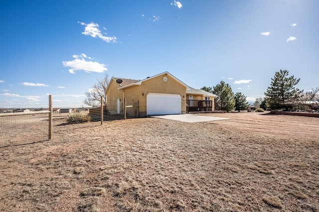 exterior space featuring concrete driveway, fence, an attached garage, and stucco siding