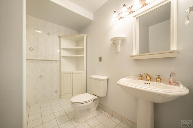 bathroom with toilet, a sink, baseboards, a tile shower, and tile patterned floors