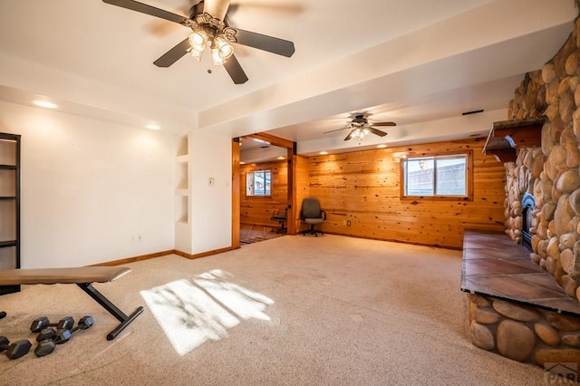 unfurnished living room with wooden walls, baseboards, ceiling fan, carpet floors, and a fireplace