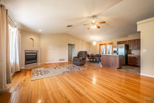 unfurnished living room with a fireplace, lofted ceiling, visible vents, light wood-style flooring, and ceiling fan