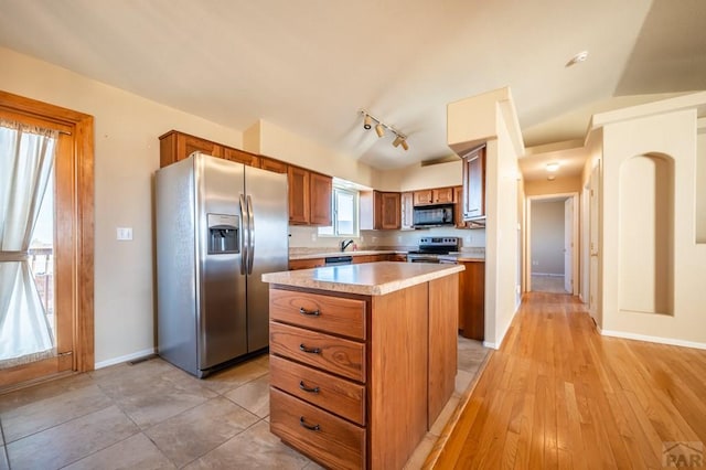 kitchen with baseboards, brown cabinetry, a kitchen island, stainless steel appliances, and light countertops