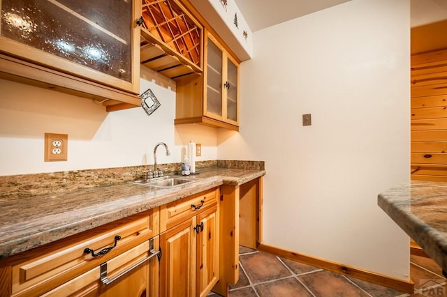 kitchen with glass insert cabinets, a sink, light stone countertops, dark tile patterned flooring, and baseboards