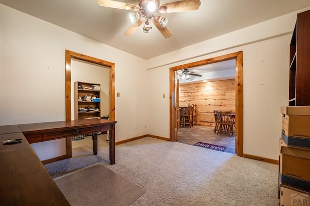 carpeted office space featuring wood walls, baseboards, and a ceiling fan