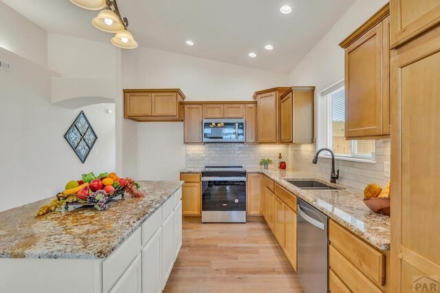 kitchen featuring light stone counters, appliances with stainless steel finishes, vaulted ceiling, and a sink