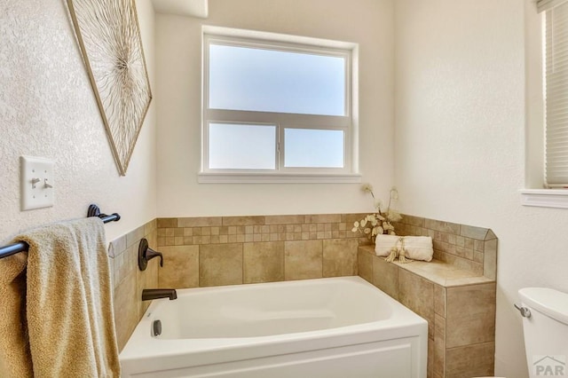 bathroom with a garden tub, toilet, and a healthy amount of sunlight