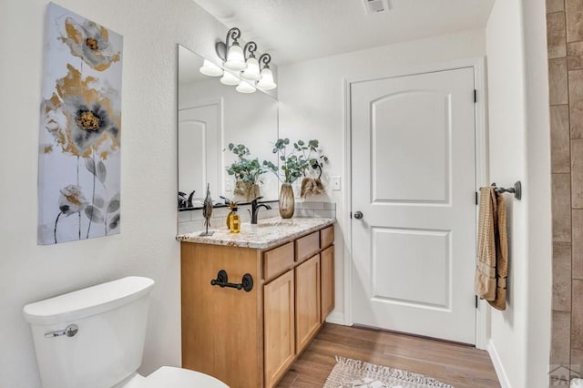 bathroom featuring visible vents, toilet, vanity, wood finished floors, and a chandelier