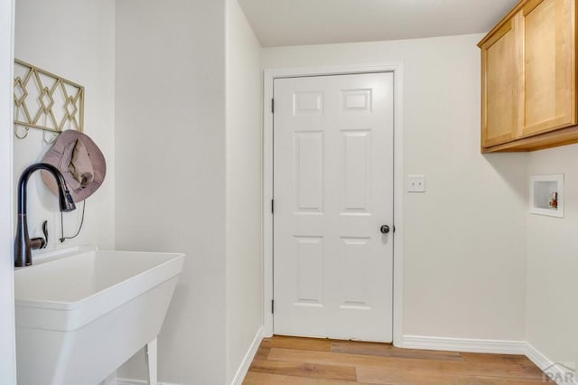 clothes washing area featuring light wood-type flooring, cabinet space, baseboards, and a sink