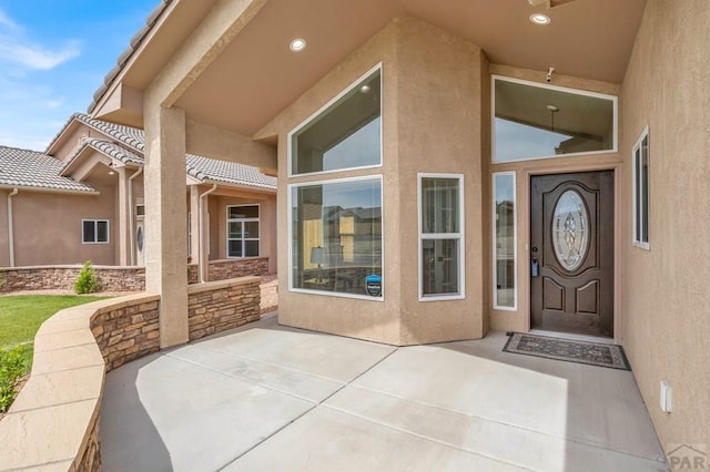 doorway to property with stone siding, a tiled roof, a patio area, and stucco siding