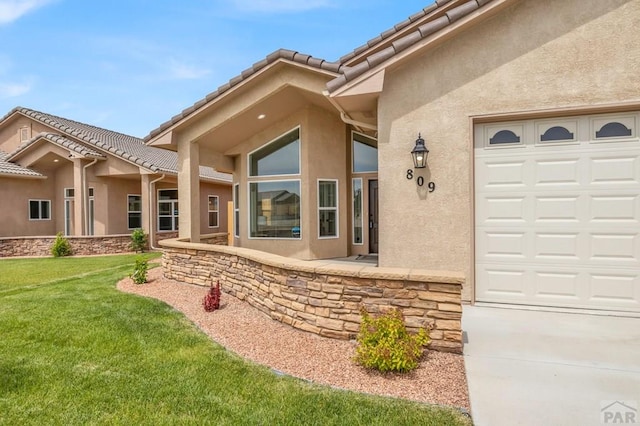 property entrance with a yard, an attached garage, a tile roof, and stucco siding