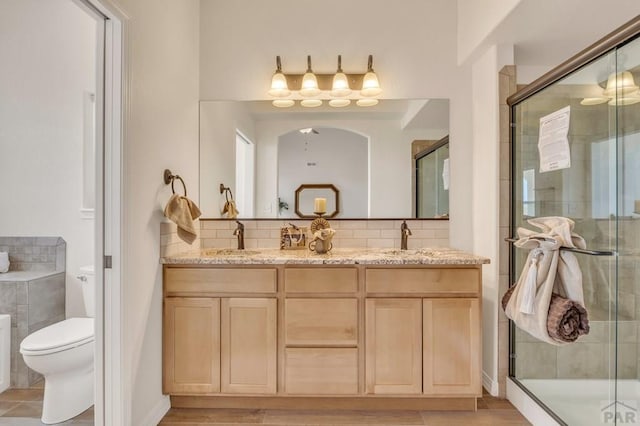 full bath with tasteful backsplash, a sink, a shower stall, and toilet