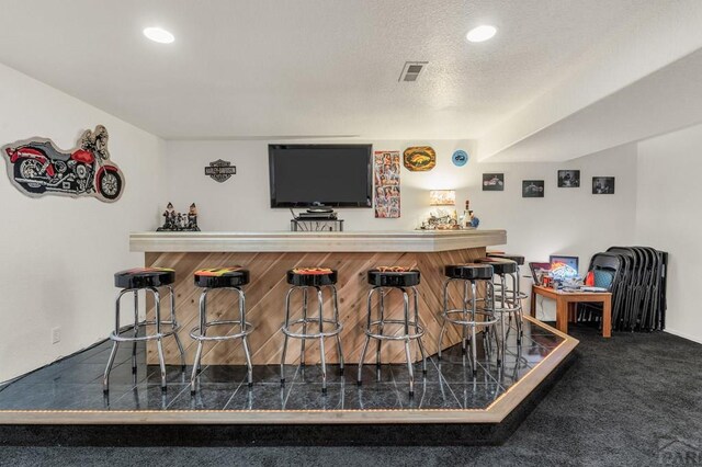 bar featuring recessed lighting, visible vents, dark carpet, a textured ceiling, and a bar