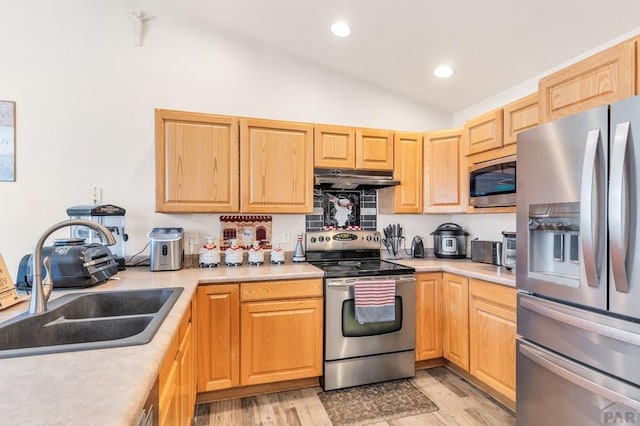 kitchen with vaulted ceiling, stainless steel appliances, light countertops, under cabinet range hood, and a sink