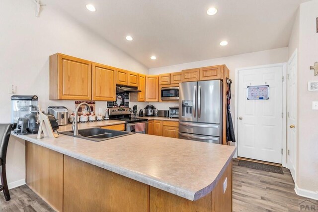 kitchen with under cabinet range hood, stainless steel appliances, a peninsula, a sink, and light countertops