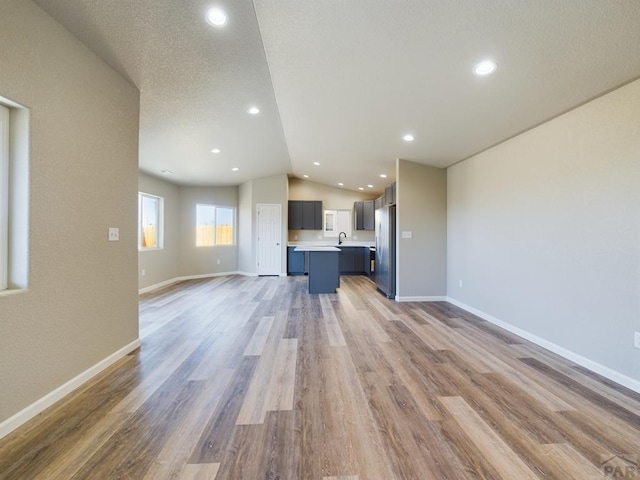 unfurnished living room featuring recessed lighting, vaulted ceiling, a sink, wood finished floors, and baseboards