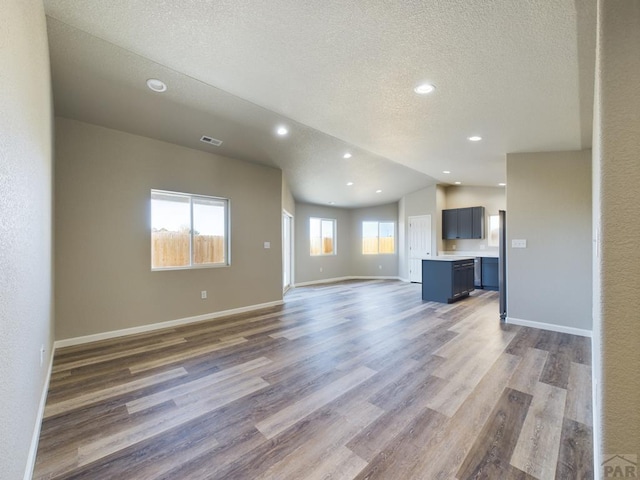 unfurnished living room with a textured ceiling, baseboards, vaulted ceiling, and dark wood-style flooring