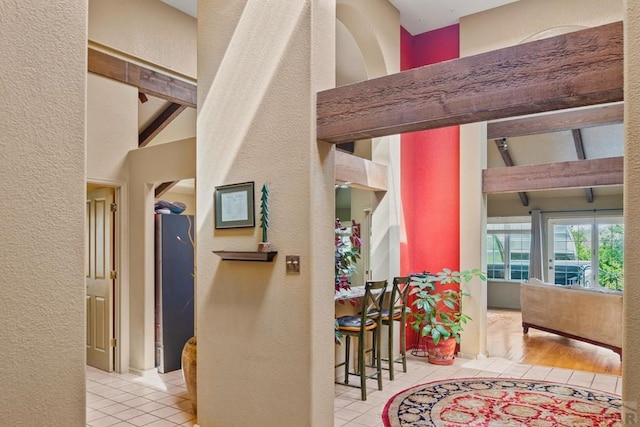 hall featuring light tile patterned floors, beam ceiling, and a textured wall