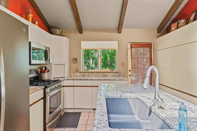 kitchen featuring light tile patterned floors, white cabinets, vaulted ceiling with beams, stainless steel appliances, and a sink