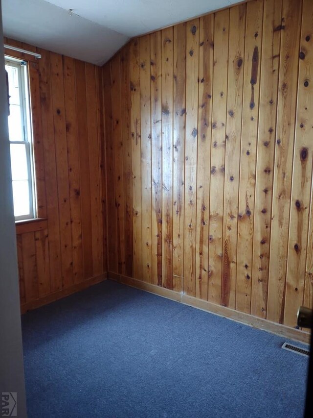 spare room with lofted ceiling, dark colored carpet, plenty of natural light, and visible vents