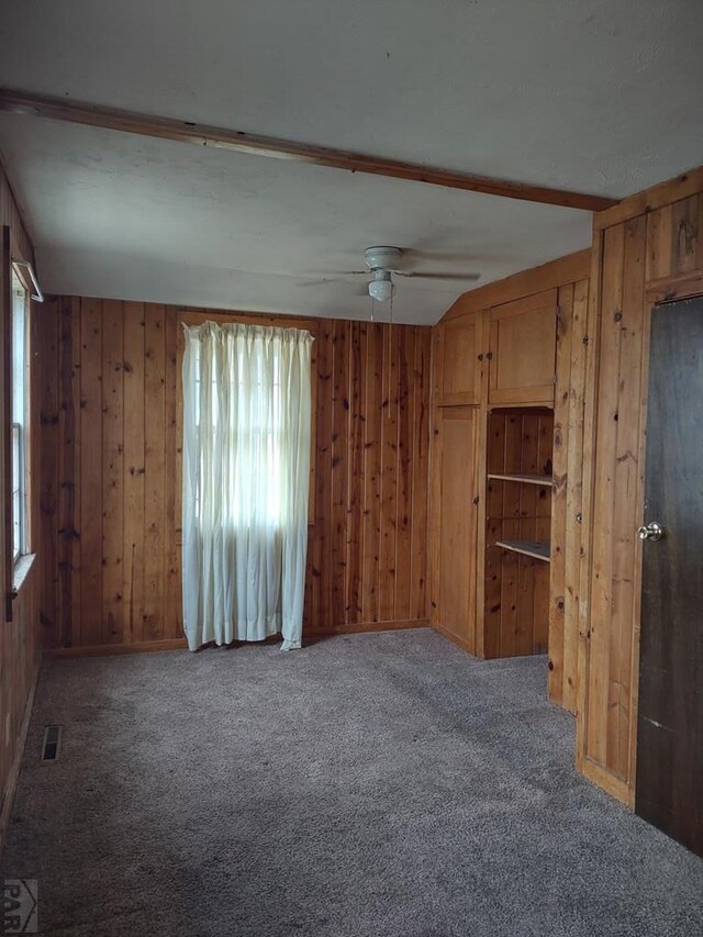 spare room with wood walls, a ceiling fan, visible vents, and carpet flooring