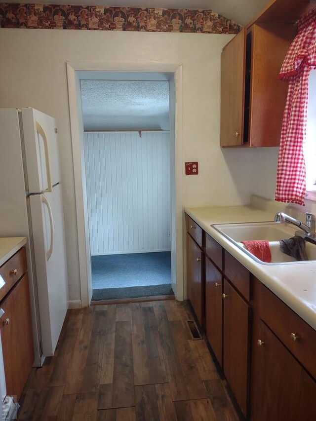 kitchen featuring dark wood-style floors, light countertops, brown cabinetry, freestanding refrigerator, and a sink