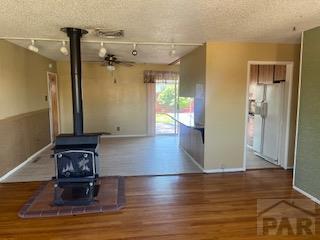 2013 Elmwood Ln, Pueblo, CO 81005 - unfurnished living room featuring a wood stove, baseboards, track lighting, a ceiling fan, and wood finished floors