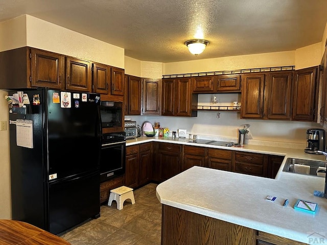 kitchen with a textured ceiling, a peninsula, a sink, light countertops, and black appliances