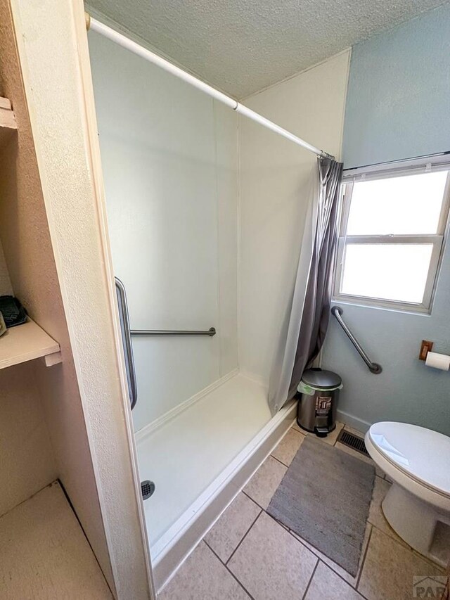 bathroom featuring a stall shower, visible vents, toilet, tile patterned floors, and a textured ceiling