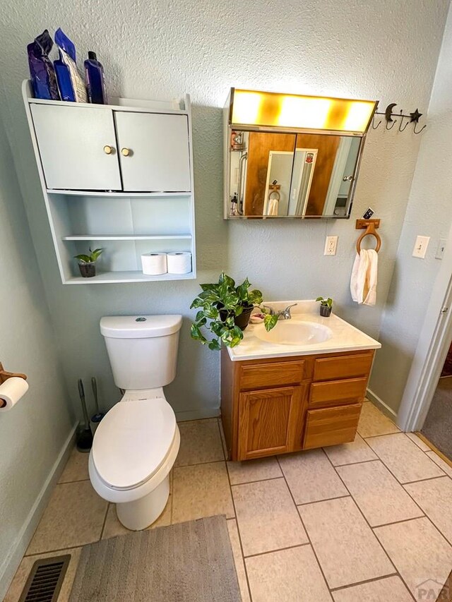 bathroom featuring toilet, vanity, baseboards, visible vents, and tile patterned floors