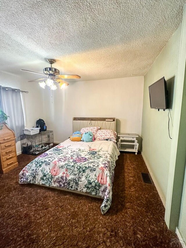 bedroom with visible vents, a textured ceiling, dark carpet, and a ceiling fan