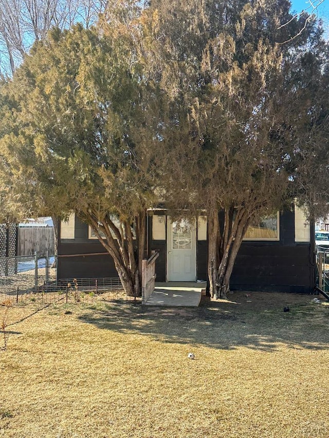 view of property hidden behind natural elements featuring a front yard and fence