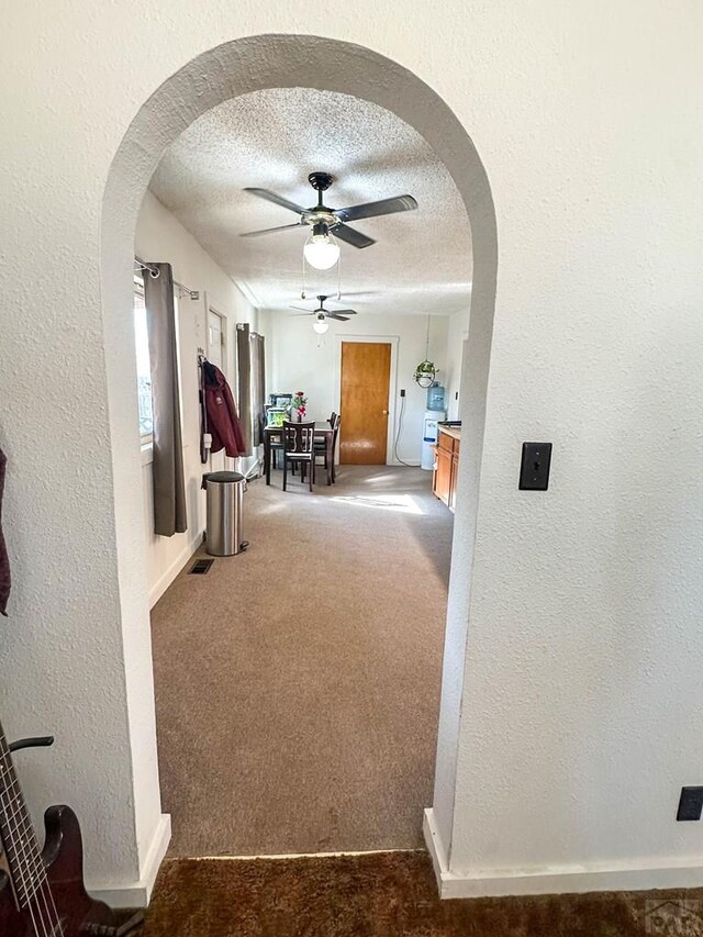 hall featuring a textured ceiling, a textured wall, arched walkways, and carpet flooring