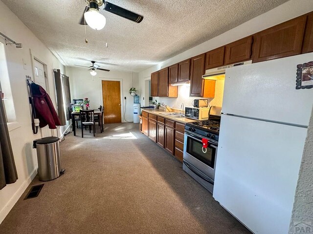 kitchen featuring light colored carpet, freestanding refrigerator, light countertops, under cabinet range hood, and gas stove