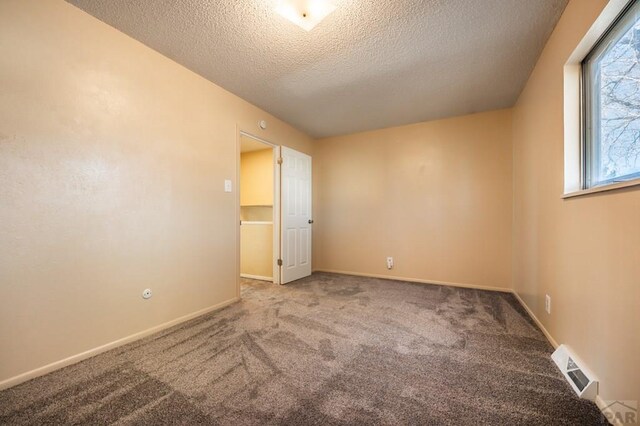 empty room featuring carpet, visible vents, a textured ceiling, and baseboards