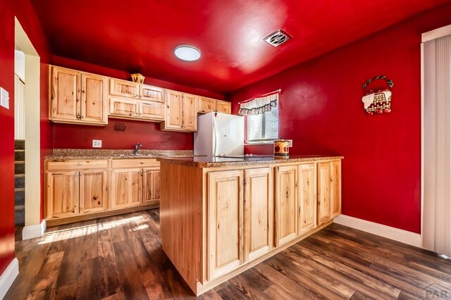 kitchen featuring visible vents, light brown cabinetry, dark wood-style flooring, and freestanding refrigerator