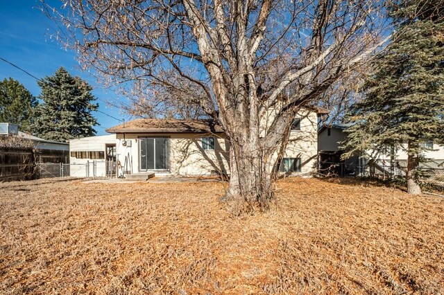 rear view of property featuring a yard, fence, and stucco siding