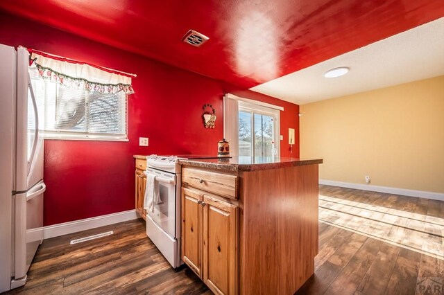 kitchen with dark wood-type flooring, dark countertops, white appliances, and baseboards