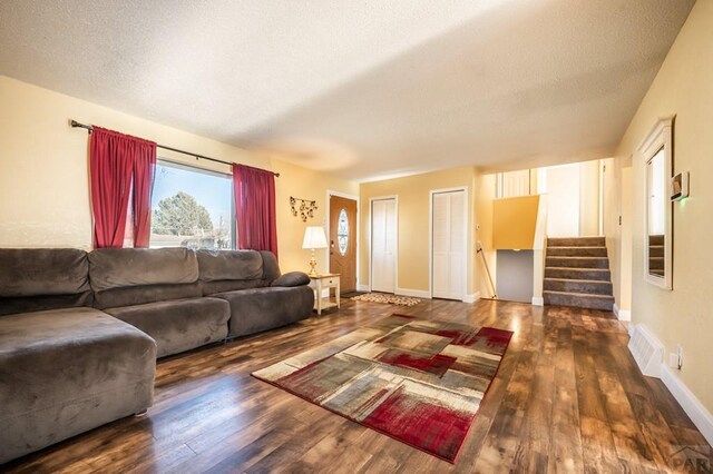 living area featuring baseboards, visible vents, stairway, dark wood-style flooring, and a textured ceiling