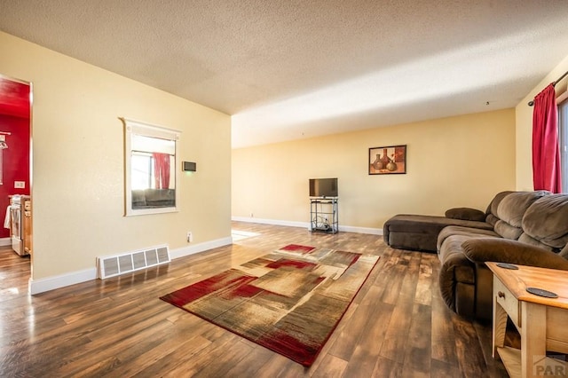 living area featuring dark wood-style flooring, visible vents, a textured ceiling, and baseboards