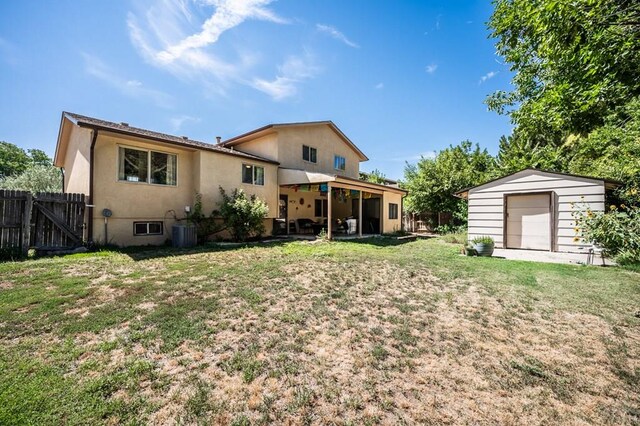 rear view of property with a yard, a detached garage, fence, a shed, and an outdoor structure