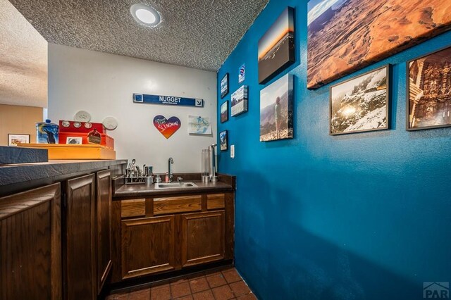 bar featuring wet bar, dark tile patterned flooring, a sink, and a textured ceiling