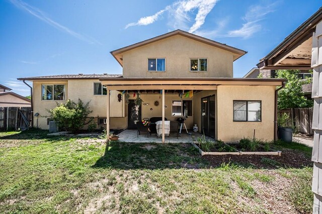 rear view of property featuring a patio, a lawn, fence, and stucco siding