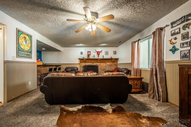 carpeted living room with a textured ceiling, wainscoting, ceiling fan, and a fireplace