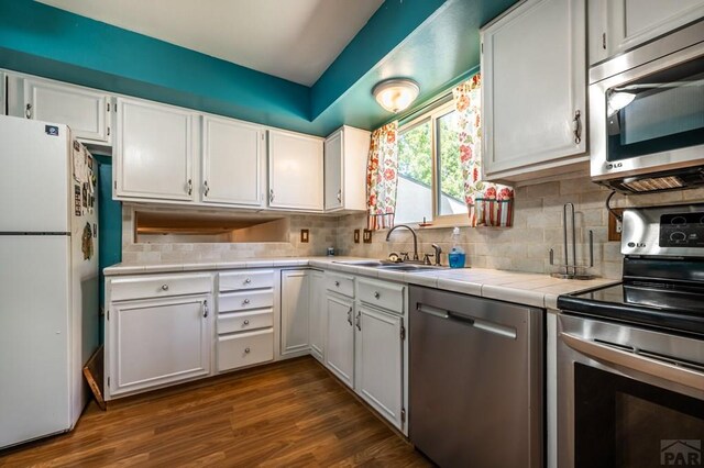 kitchen with decorative backsplash, tile countertops, stainless steel appliances, white cabinetry, and a sink