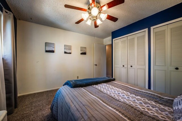 unfurnished bedroom featuring baseboards, ceiling fan, a textured ceiling, dark carpet, and multiple closets