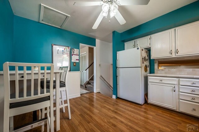 kitchen with light countertops, light wood-type flooring, freestanding refrigerator, and white cabinets