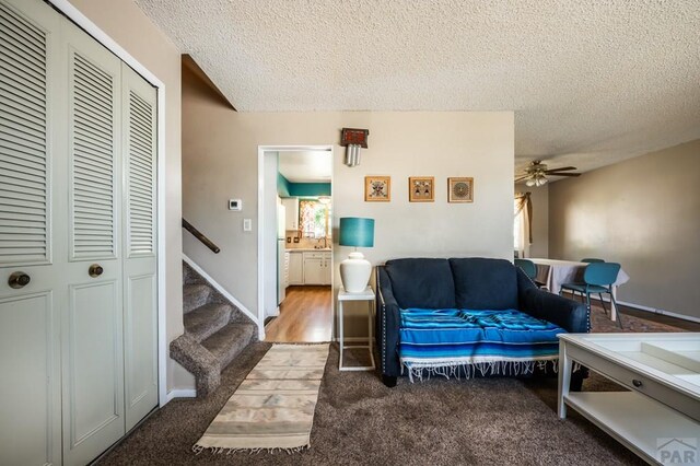 living area with baseboards, a ceiling fan, stairway, carpet, and a textured ceiling