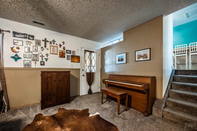 sitting room with light colored carpet, visible vents, a textured ceiling, and stairs