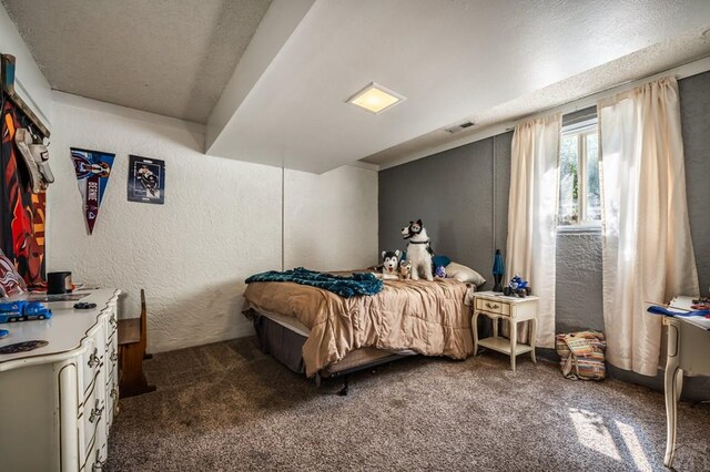 bedroom with dark colored carpet, visible vents, and a textured wall