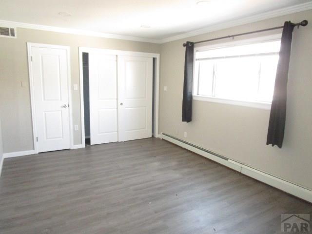 unfurnished bedroom with a baseboard heating unit, ornamental molding, a closet, and dark wood finished floors