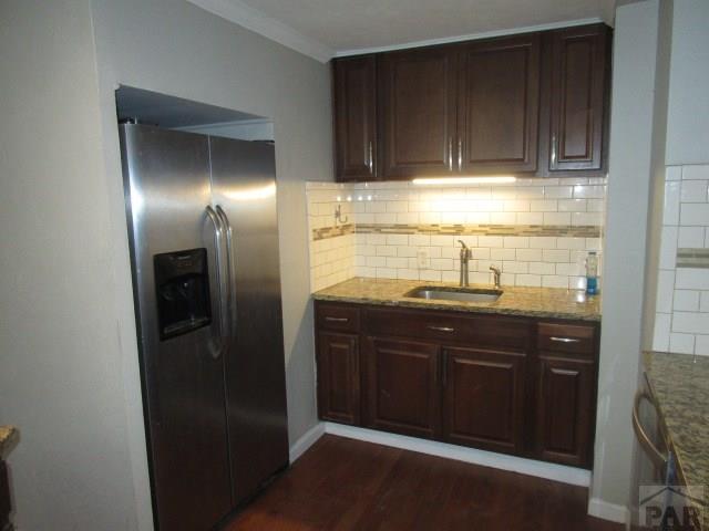 kitchen featuring light stone counters, dark wood-type flooring, a sink, stainless steel refrigerator with ice dispenser, and decorative backsplash